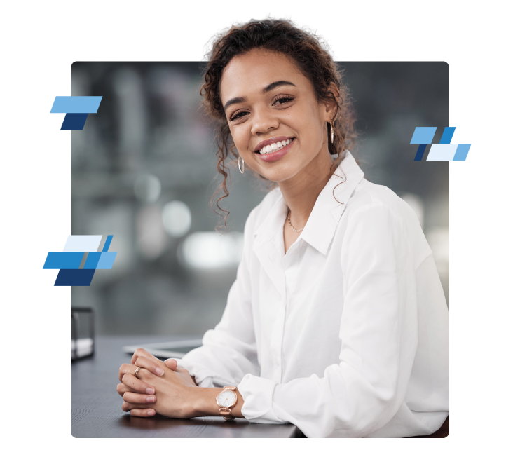 cta-4 A woman with curly hair smiles warmly, wearing a white blouse. She is seated at a table with her hands clasped, perhaps discussing the benefits of Freight Agent Software. The background is softly blurred, and there are abstract blue shapes around her.