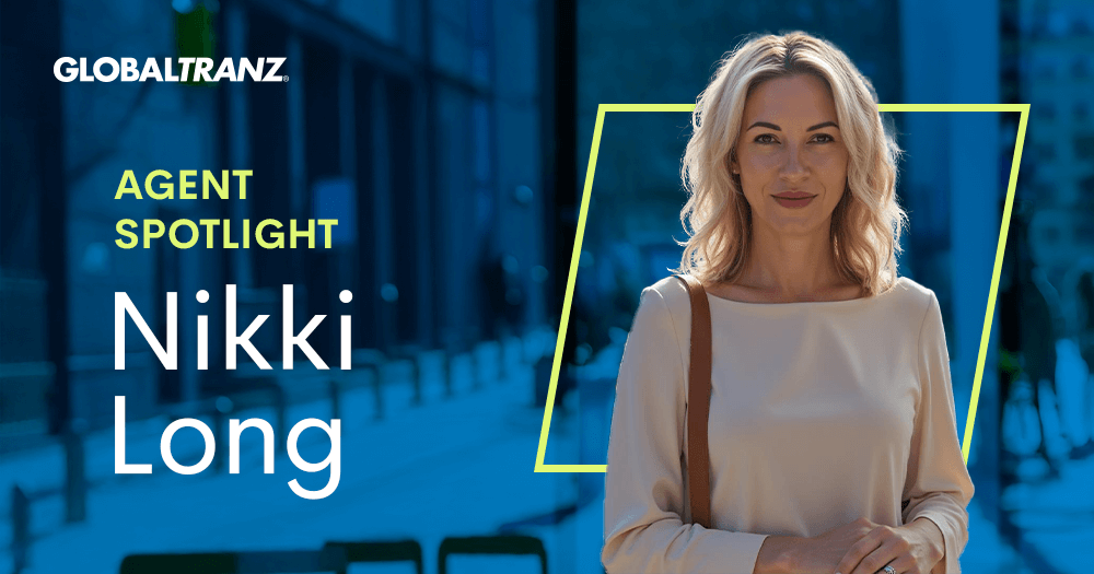 A woman with blonde hair stands outdoors, smiling. Text reads: GLOBALTRANZ. Agent Spotlight. Nikki Long. The background is blurred, showing a city street with sunlight and blue tones.
