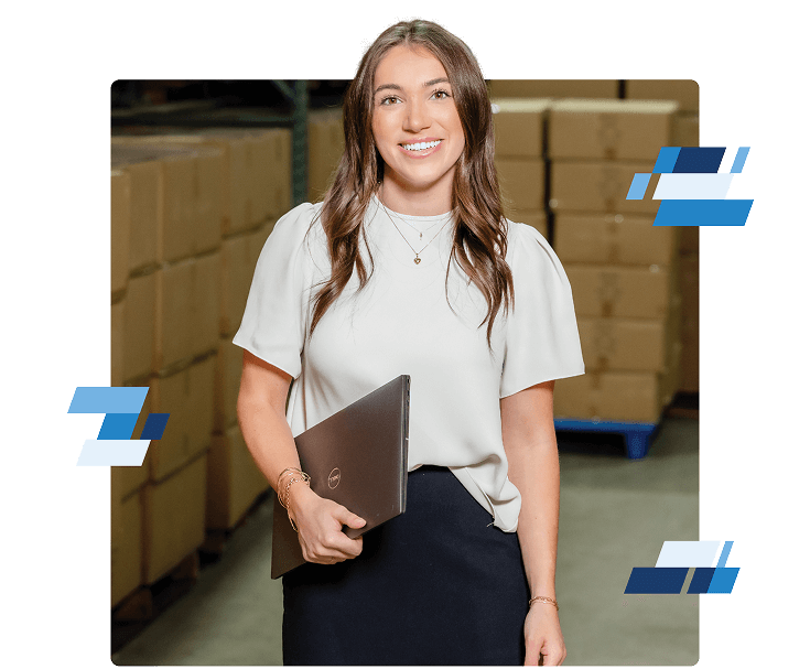 Freight Agent Culture5 A woman with long brown hair, wearing a white blouse and black skirt, smiles while holding a closed laptop. She stands in a warehouse with stacked cardboard boxes in the background. Blue graphic elements decorate the image.