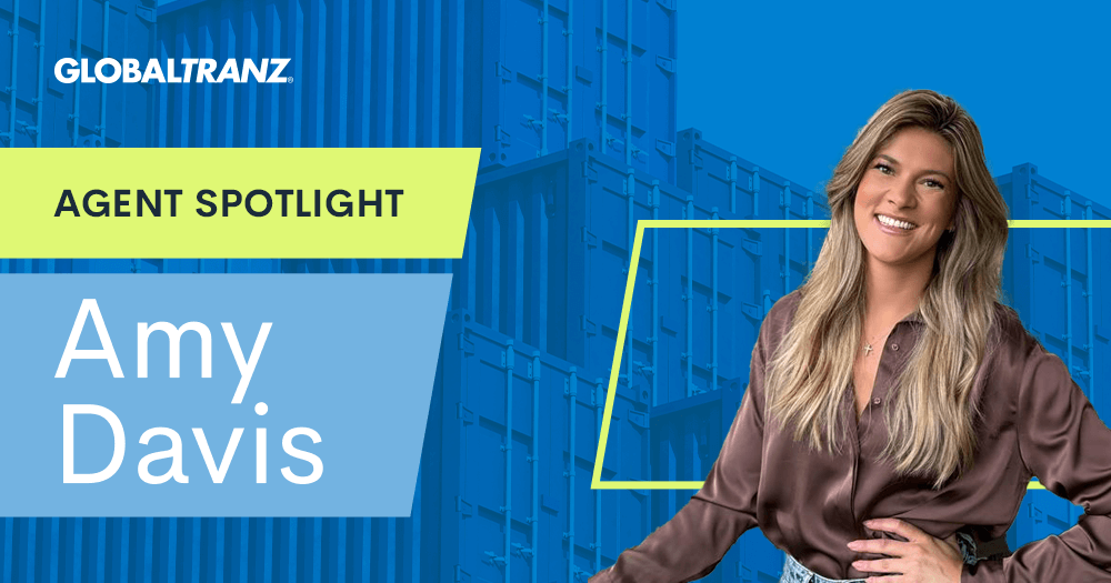 A woman with long blonde hair and a brown blouse smiles in front of a background with shipping containers. Text reads: GLOBALTRANZ. AGENT SPOTLIGHT. Amy Davis.