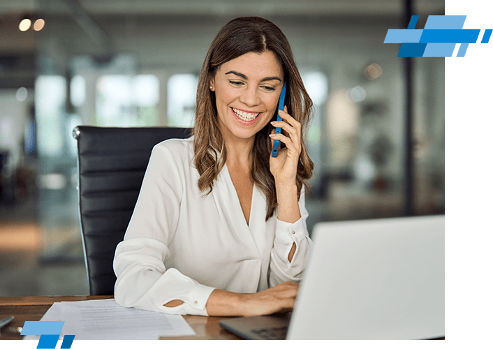 A smiling woman in a white blouse sits at a desk, talking on her phone and using a laptop. Papers are on the desk, and she appears to be in a modern office setting, perhaps reviewing details from a salary calculator. Blue graphic elements decorate the image.